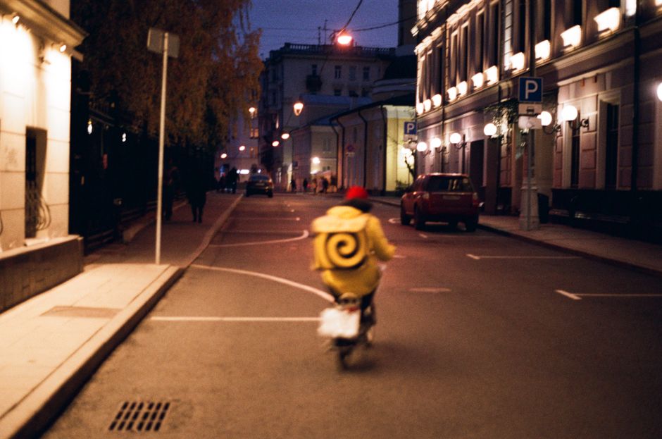 A cyclist rides through a dimly lit urban street at night, passing by illuminated buildings.